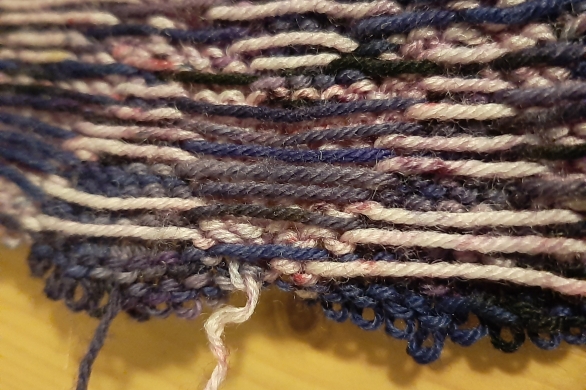 The reverse of purple colourwork knitting being unraveled
